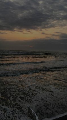 the sun is setting over the ocean with waves coming in to shore and dark clouds