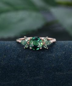 a green ring with three stones on it's side and leaves in the background