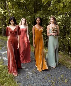 four women in long dresses standing on gravel path with trees in the backgroud