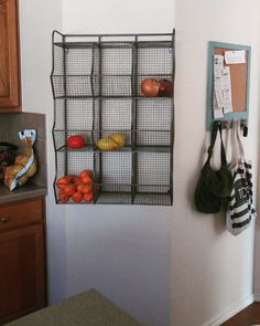 a metal rack holding fruit and vegetables next to a wall mounted shelf with hooks on it