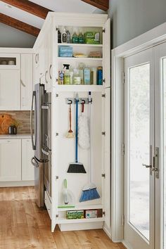 an organized kitchen with white cabinets and wooden floors, including brooms and mop's