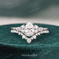 an engagement ring with a pear shaped diamond surrounded by small round brilliant cut diamonds on a green velvet box