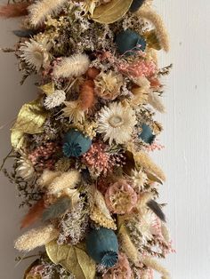 an arrangement of dried flowers and leaves on a wall