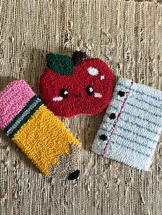 two knitted objects are laying on the floor next to an apple, pencil and eraser