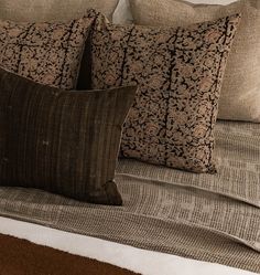 three pillows on top of a bed with brown and white linens, one in the foreground