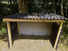 a wooden structure with a metal roof in the middle of some grass and trees behind it