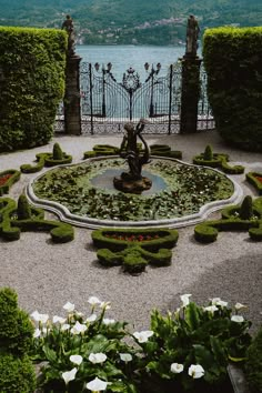 a fountain surrounded by plants and flowers in the middle of a garden with a lake in the background