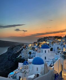 the sun is setting over an island with white buildings and blue domes in the foreground