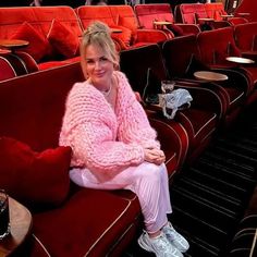 a woman in pink sweater and white pants sitting on a red couch