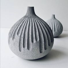 two gray vases sitting next to each other on a white counter top, one is shaped like a shell