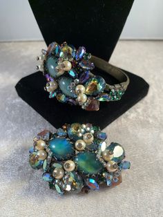 "This is an extremely rare and beautiful SPARKLING Hobé brooch and bracelet demi parure fully encrusted in large and small saphiret glass cabochons/stones that exhibit turquoise-pink-brown tones. All pieces are accented with rhinestone topped pearls and small green and round rhinestones and several blue-green metallic finished navettes! The other quite unique addition are the small arrow-shaped clusters of tiny AB rhinestones surrounding the pearls that move freely. It really is such a beautiful set, and must be seen in person to appreciate - I tried to capture the beauty of the saphiret stones which is difficult to do in a picture. The glass was made in the first half of the century by adding gold to sapphire blue glass (the earlier the piece the pinker tone of the stone), creating beauti Vintage Gemstone Jewelry For Party, Multicolor Brooch Jewelry For Evening, Multicolor Brooch For Evening Wear, Antique Multicolor Brooch Jewelry, Collectible Iridescent Cabochon Jewelry, Unique Collectible Jeweled Jewelry, Iridescent Brooch Jewelry Gift, Iridescent Brooch Jewelry For Gifts, Vintage Iridescent Gemstone Jewelry