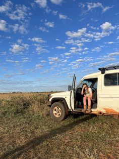 two people sitting in the back of a truck on top of a dry grass field