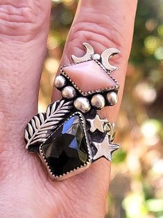 Black spinel and pink opal gothic sterling silver ring. Handmade with sterling silver sheet and wire sourced in the united states. This beautiful multi stone ring is a one of a kind unique piece, features a teardrop black spinel cabochon and a geometric pink opal, 6 handmade sterling silver beads in various sizes 1 small star and 1 pattern star 2 moons a cast ferm leaf and a star ring shank size 8.  Ring design is about 1.6 inches long x 1 inch wide.  Ready to ship. Handmade Pink Gothic Jewelry, Mystical Black Sterling Silver Rings, Black Spinel Ring, 2 Moons, Spinel Ring, Ring Shank, Star Ring, Black Spinel, Higher Self