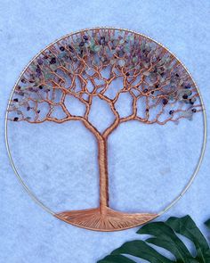 a metal wire tree with leaves and beads in the shape of a circle on a white background