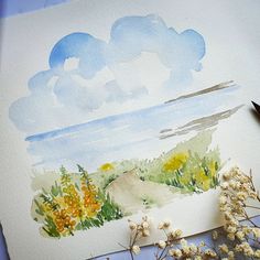 a watercolor painting with flowers and clouds in the sky on paper next to paintbrushes