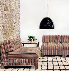 a living room with two couches and a rug on the floor in front of a stone wall