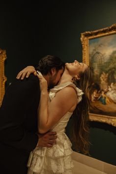 a man and woman kissing in front of a painting