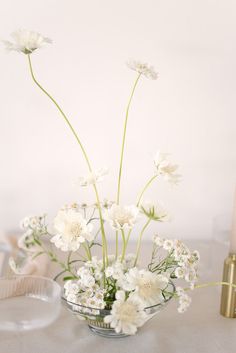 white flowers in a glass vase on a table next to a candle and some candles