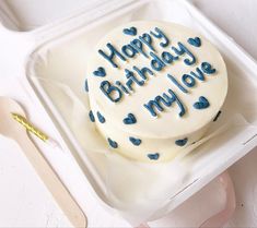 a birthday cake with blue writing on it in a plastic container next to utensils