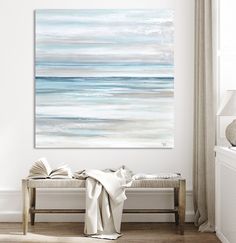 a white and blue painting on the wall above a bench with a blanket draped over it