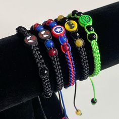 five bracelets with different colored beads and designs on them sitting on a black stand