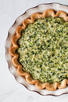 a quiche with spinach and cheese in a pie dish on a white table