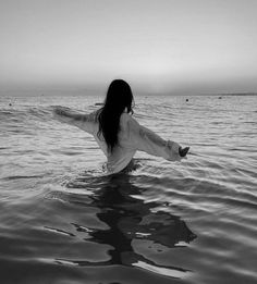 a woman is standing in the water with her arms spread out and she's back to the camera