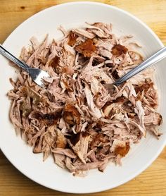 a white bowl filled with shredded meat on top of a wooden table next to a fork