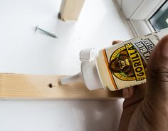 a hand holding a bottle of glue next to a window sill with a screwdriver on it