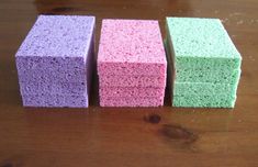 three different colored sponges sitting on top of a wooden table