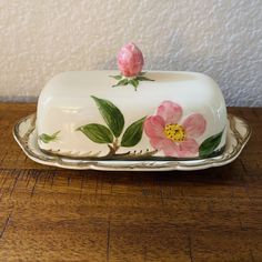 a white cake with pink flowers on it sitting on a wooden table next to a wall