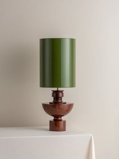 a green lamp sitting on top of a table next to a white cloth covered wall