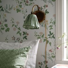 a green lamp hanging from the side of a wall next to a bed with pillows