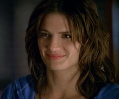 a woman with long brown hair and blue shirt smiles at the camera while standing in a dark room