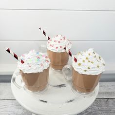 three iced coffees with whipped cream and sprinkles are on a white plate