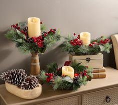 christmas decorations on a dresser with pine cones, holly berries and candles in the center