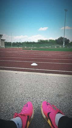 a person's feet in pink shoes on a track with an empty field behind them