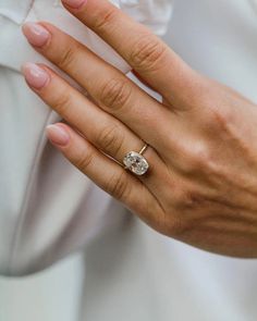 a woman's hand with a ring on it and a white shirt in the background