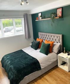 a bedroom with green and orange pillows on the headboard, white bedding and wooden flooring