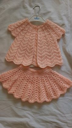 two crocheted baby sweaters sitting on top of a bed