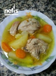 a white bowl filled with chicken and carrots on top of a marble countertop