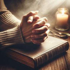 a person holding their hands on top of a book with a candle in the background