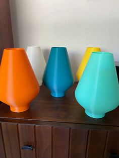 four different colored vases sitting on top of a wooden cabinet