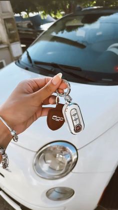 a hand holding a car key in front of a white car