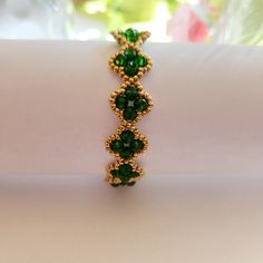 a green bracelet is sitting on a white surface with flowers in the background and a window behind it