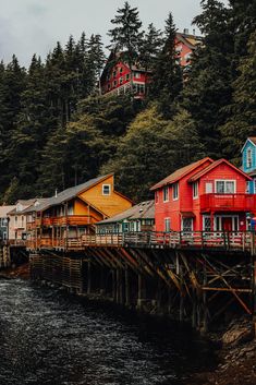 colorful houses line the shore of a body of water in front of trees and mountains