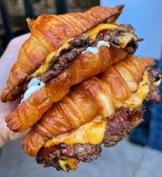 a croissant sandwich with meat and cheese on it being held in someone's hand