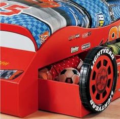 a red race car bed with wheels on it's sides and storage underneath the bed