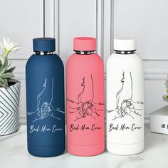 three different colored water bottles sitting next to each other on a white counter with plants in the background