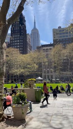 people are sitting and walking around in the park with tall buildings on either side of them